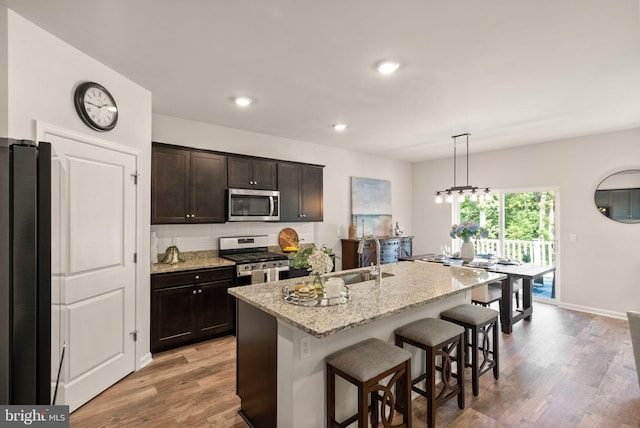 kitchen with light wood-type flooring, appliances with stainless steel finishes, sink, an island with sink, and a breakfast bar