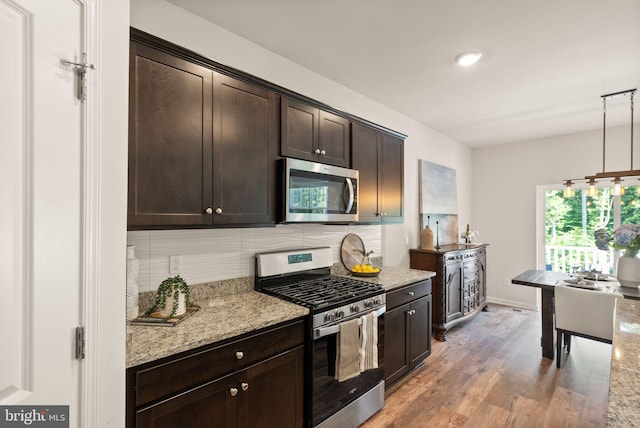 kitchen with dark brown cabinetry, decorative backsplash, light wood-style flooring, light stone counters, and stainless steel appliances