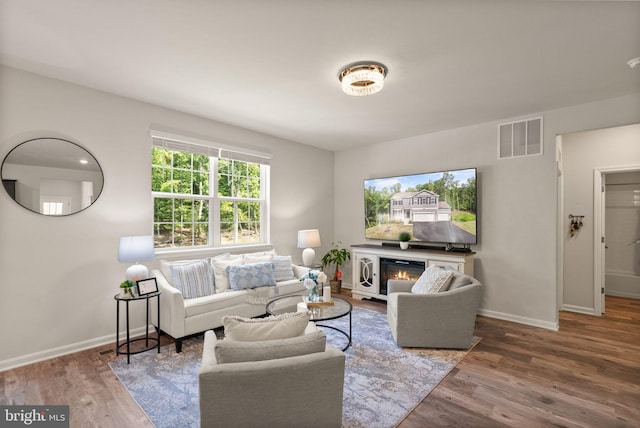 living area with a glass covered fireplace, visible vents, baseboards, and wood finished floors