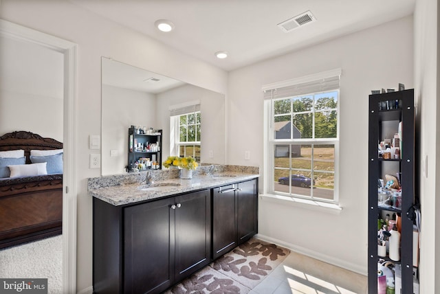 kitchen featuring baseboards, visible vents, light stone counters, and a sink