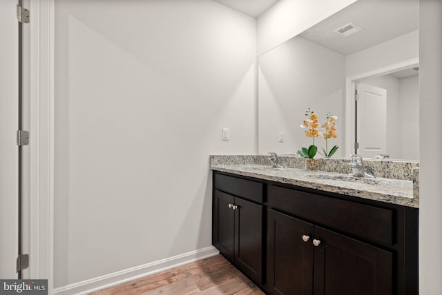 bathroom featuring a sink, double vanity, wood finished floors, and baseboards