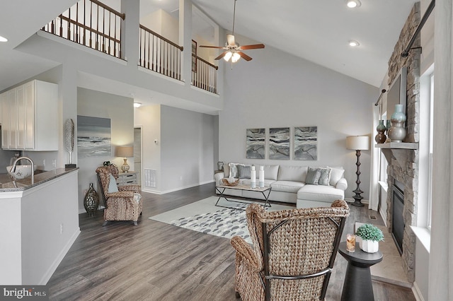 living room with high vaulted ceiling, a stone fireplace, sink, wood-type flooring, and ceiling fan