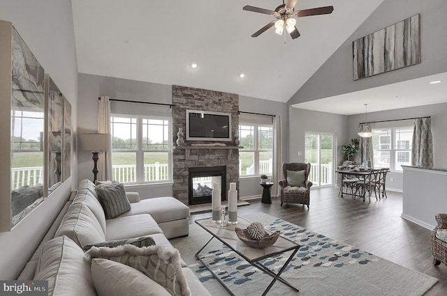 living room with a wealth of natural light, high vaulted ceiling, hardwood / wood-style floors, and a stone fireplace