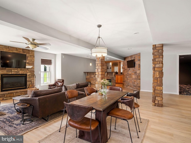 dining room with light hardwood / wood-style flooring, ceiling fan, a stone fireplace, and decorative columns