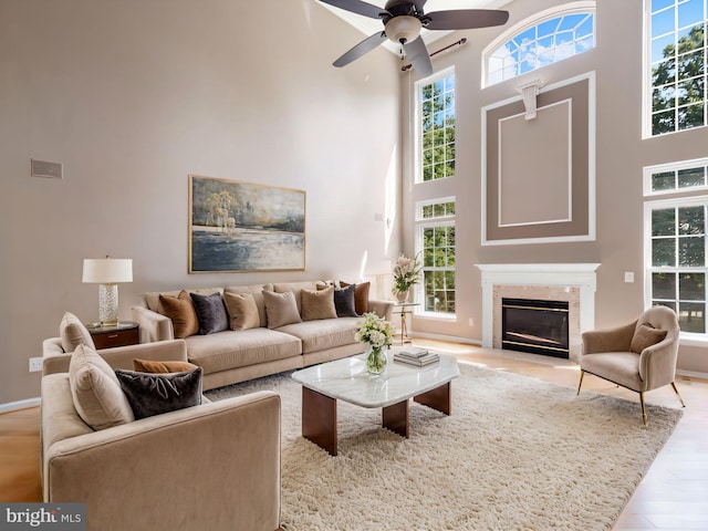 living room featuring ceiling fan, light hardwood / wood-style floors, a towering ceiling, and a fireplace