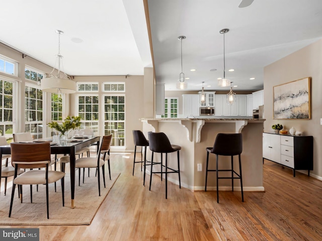 kitchen with light hardwood / wood-style floors, white cabinetry, a kitchen bar, light stone counters, and hanging light fixtures