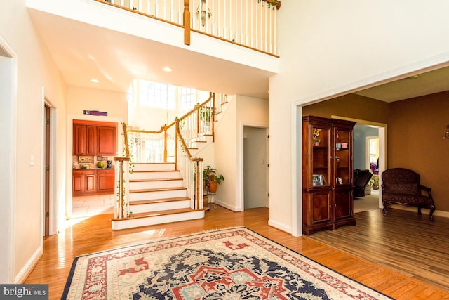 foyer entrance featuring stairs, a high ceiling, light wood-style flooring, and baseboards