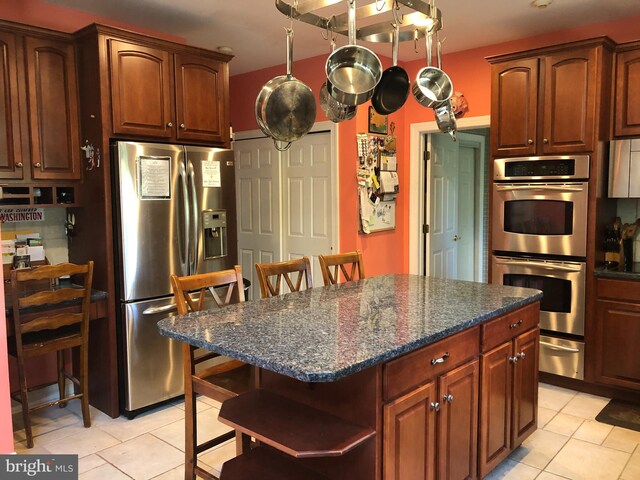 kitchen with dark stone countertops, light tile patterned floors, stainless steel appliances, a kitchen breakfast bar, and a center island