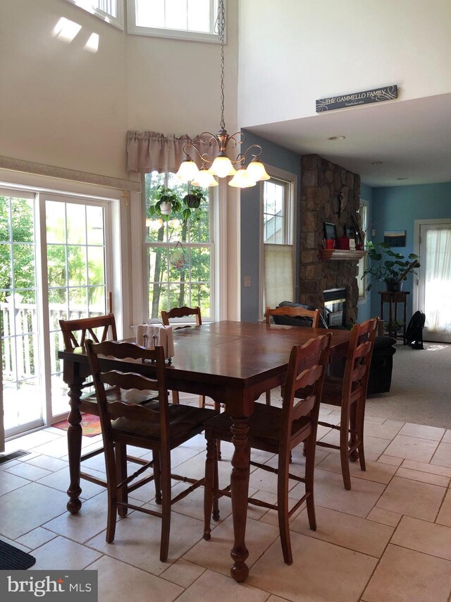 dining room with a high ceiling, light tile patterned floors, a chandelier, and a stone fireplace