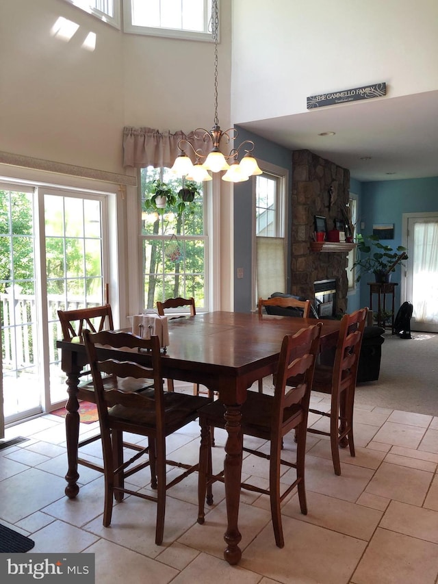 dining room featuring a notable chandelier, a fireplace, a towering ceiling, and a healthy amount of sunlight