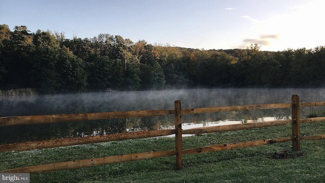 view of water feature featuring a wooded view and fence