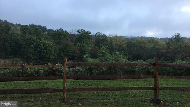 view of gate with a lawn, fence, and a wooded view