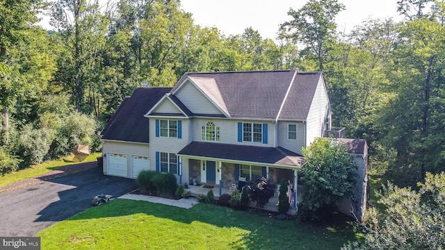 view of front facade featuring a porch, a view of trees, a front lawn, and aphalt driveway