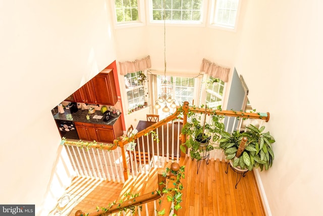 stairway with a towering ceiling, a notable chandelier, baseboards, and wood finished floors