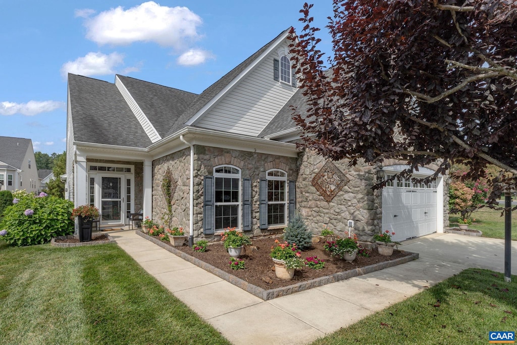 view of front of home featuring driveway, a shingled roof, stone siding, an attached garage, and a front yard