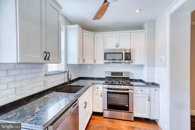 kitchen featuring light wood-type flooring, white cabinetry, appliances with stainless steel finishes, sink, and dark stone countertops