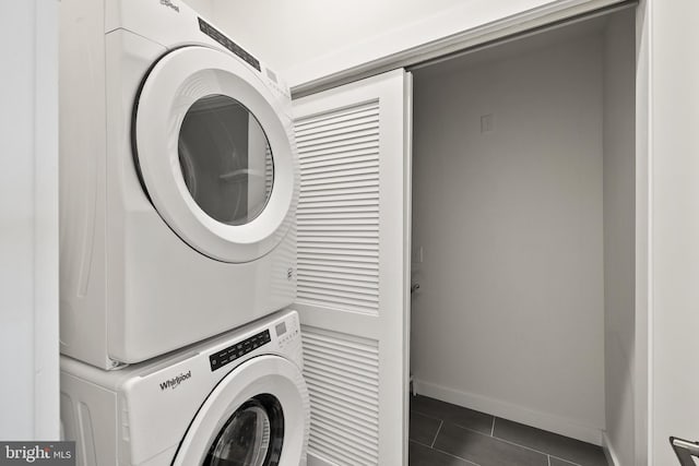 washroom with stacked washer and dryer and dark tile patterned floors