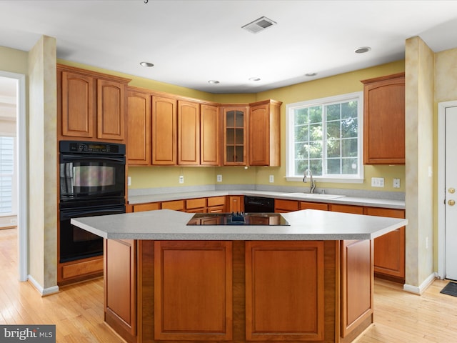 kitchen with black appliances, light hardwood / wood-style floors, a kitchen island, and sink