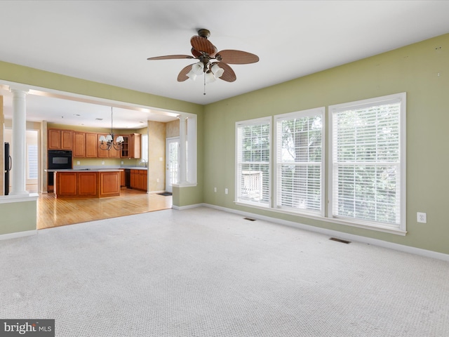 unfurnished living room with ceiling fan with notable chandelier, light hardwood / wood-style floors, and ornate columns