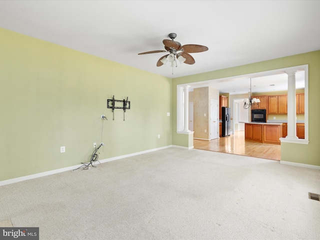 spare room featuring ceiling fan with notable chandelier, decorative columns, and light colored carpet