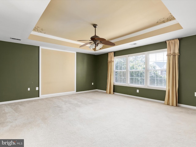 carpeted spare room featuring a tray ceiling, ceiling fan, and crown molding