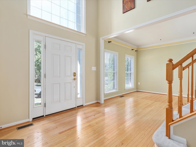 foyer with ornamental molding, light wood-type flooring, a towering ceiling, and plenty of natural light