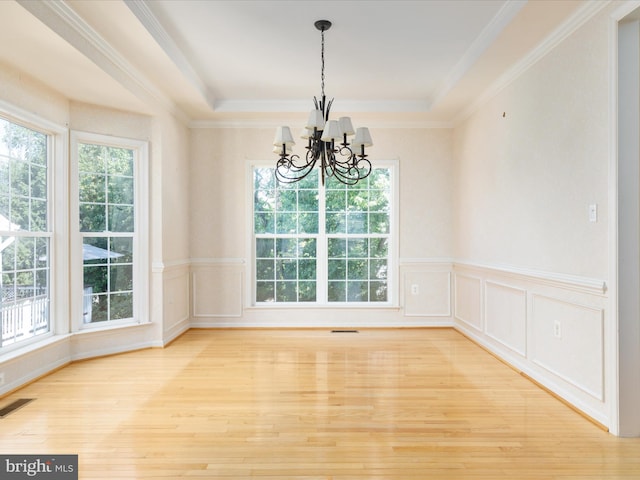 unfurnished dining area with ornamental molding, an inviting chandelier, a tray ceiling, and light hardwood / wood-style floors