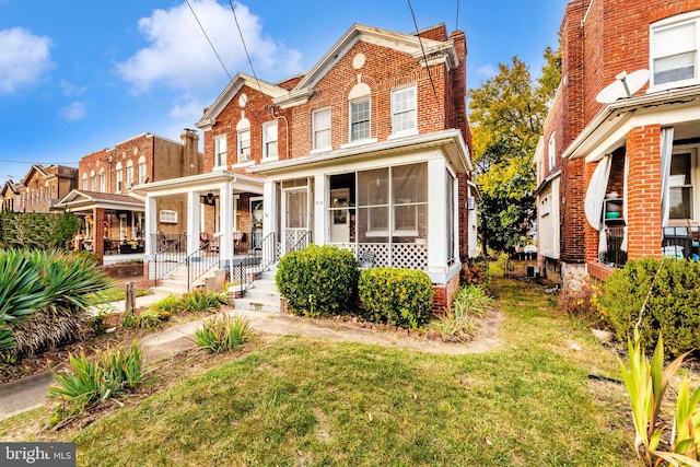 multi unit property featuring covered porch, a front lawn, and a sunroom