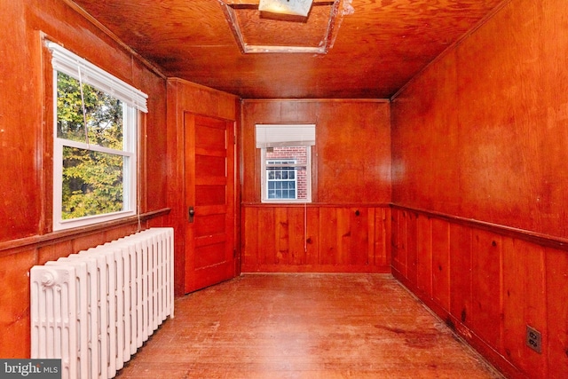 empty room with light hardwood / wood-style flooring, wood walls, wooden ceiling, and radiator