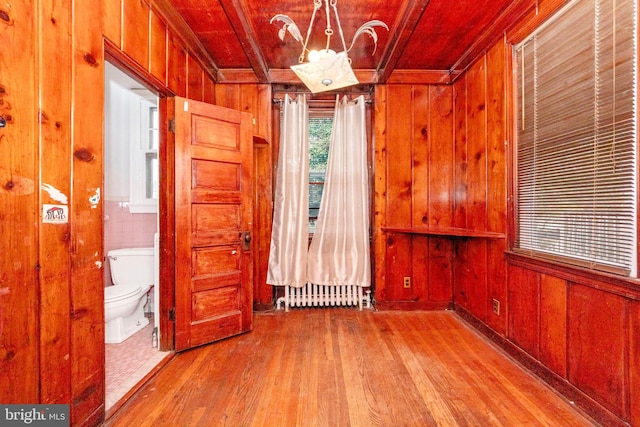 empty room featuring wood walls, radiator heating unit, light wood-type flooring, and a notable chandelier