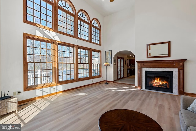 living area with arched walkways, baseboards, light wood finished floors, and a tile fireplace