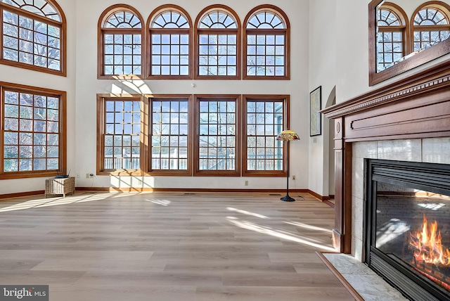 unfurnished living room with light wood-style floors, a tile fireplace, a high ceiling, and baseboards