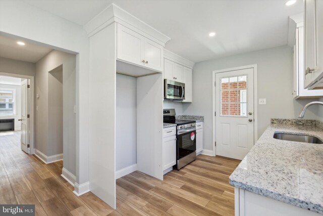 kitchen with appliances with stainless steel finishes, white cabinets, light wood-type flooring, and sink