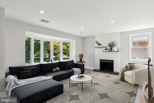 living room with light hardwood / wood-style floors, a large fireplace, plenty of natural light, and brick wall