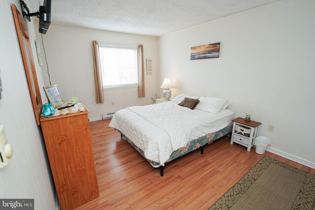 bedroom featuring baseboard heating, light hardwood / wood-style floors, and a textured ceiling