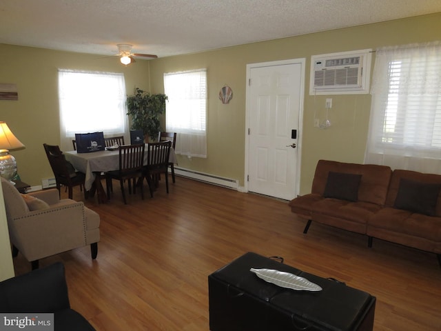 living room featuring a wall mounted air conditioner, baseboard heating, wood-type flooring, and ceiling fan