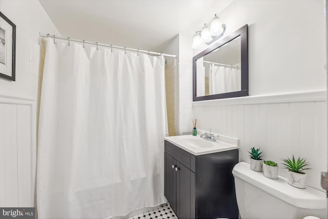 bathroom with a shower with shower curtain, wainscoting, vanity, and toilet