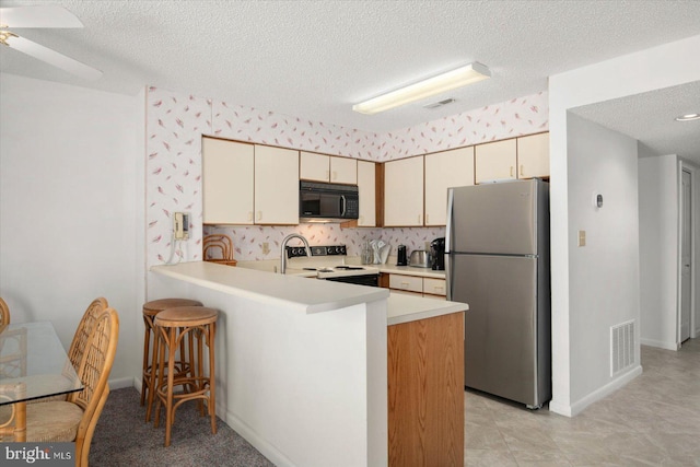 kitchen with cream cabinetry, white range with electric stovetop, kitchen peninsula, stainless steel fridge, and ceiling fan