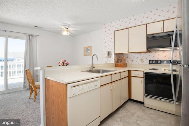 kitchen featuring cream cabinetry, light countertops, a sink, white appliances, and a peninsula