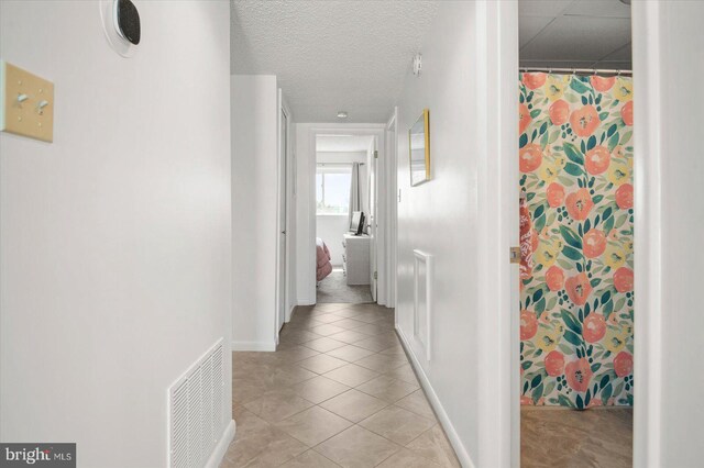 corridor with a textured ceiling and light tile patterned flooring