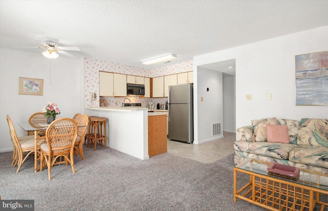 kitchen with ceiling fan, light colored carpet, stainless steel refrigerator, cream cabinetry, and kitchen peninsula