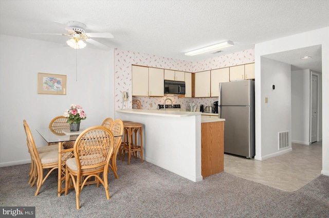 kitchen with black microwave, cream cabinets, a peninsula, light countertops, and freestanding refrigerator