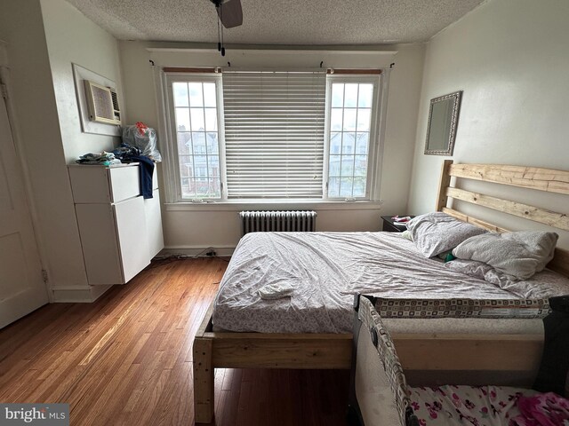 bedroom with ceiling fan, light wood-type flooring, radiator heating unit, a textured ceiling, and a wall mounted air conditioner