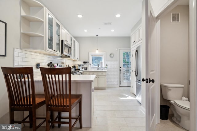 kitchen featuring white cabinetry, kitchen peninsula, pendant lighting, light tile patterned flooring, and appliances with stainless steel finishes