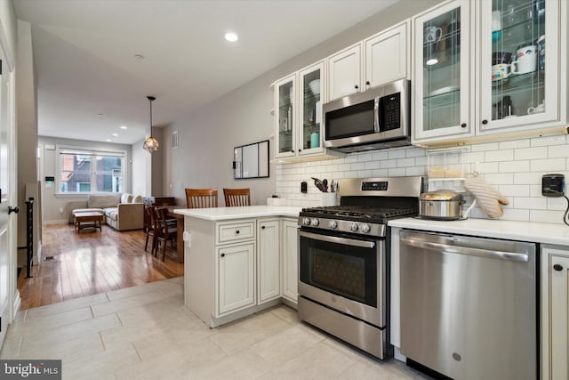 kitchen with pendant lighting, white cabinets, light hardwood / wood-style flooring, kitchen peninsula, and stainless steel appliances