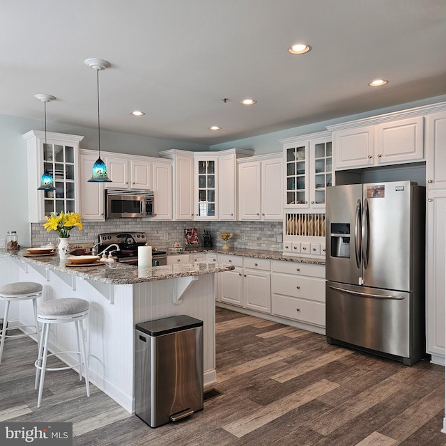 kitchen featuring backsplash, stainless steel appliances, light stone countertops, white cabinets, and dark wood-type flooring