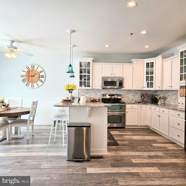 kitchen featuring stainless steel appliances, white cabinetry, hardwood / wood-style flooring, and light stone countertops