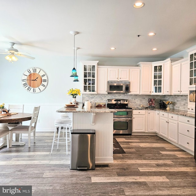 kitchen featuring stainless steel appliances, hanging light fixtures, a kitchen bar, and glass insert cabinets