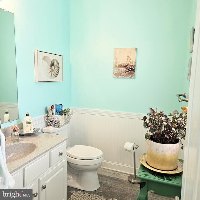 bathroom featuring toilet, a wainscoted wall, wood finished floors, and vanity