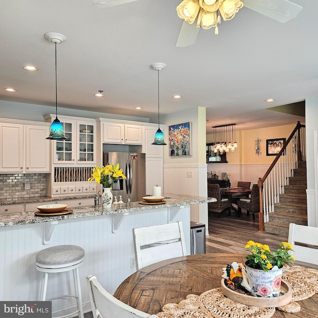 kitchen with decorative light fixtures, white cabinetry, stainless steel refrigerator with ice dispenser, light stone countertops, and ceiling fan